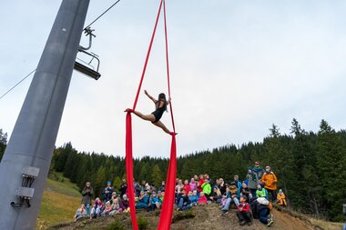 Künstlerin beim Kunterbunt Festival im Brandnertal | © Bergbahnen Brandnertal, Bettina Schwarzhans Vertikaltuchkünstlerin schwebt über Publikum auf dem Wanderweg. | © Bergbahnen Brandnertal, Bettina Schwarzhans